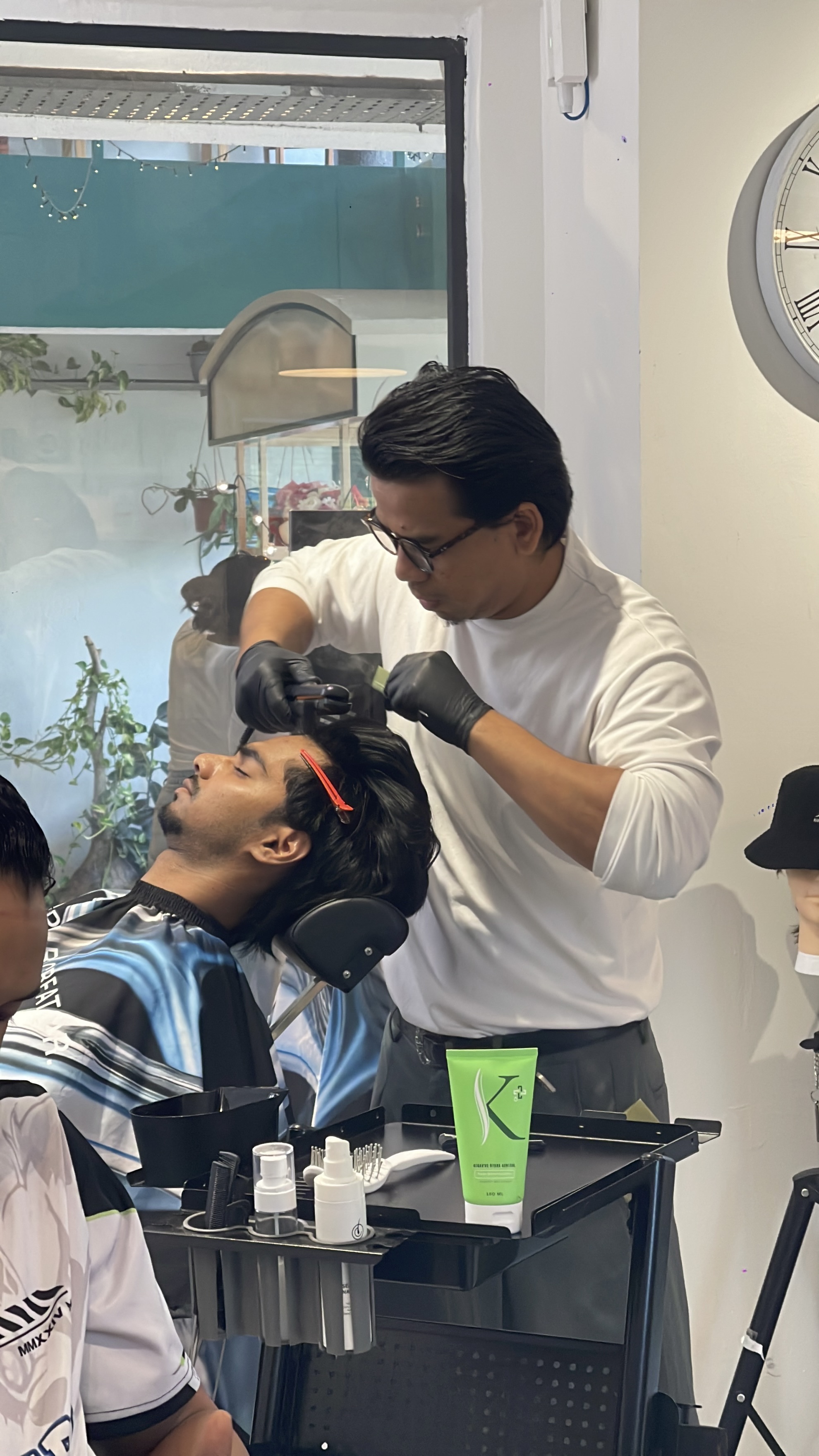 A barber carefully working on a reclining client’s hair at The Brozkey Club