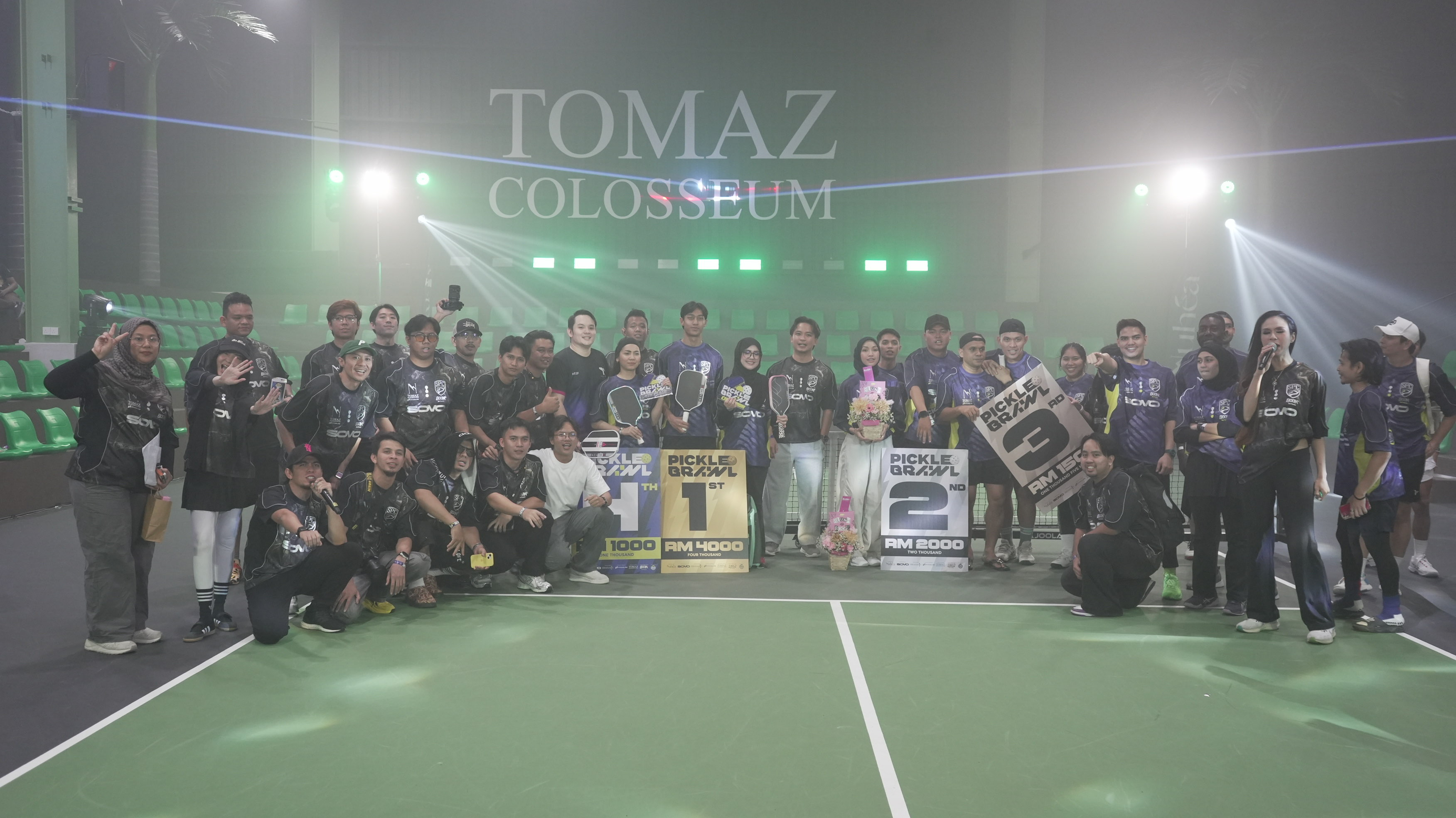 Picklebrawl participants gathered on the court with prize boards beneath the TOMAZ Colosseum sign